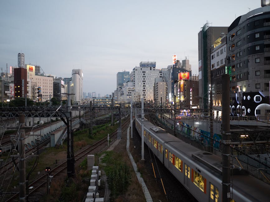 Train journey through Tokyo at dusk with illuminated cityscape surrounding railway tracks.